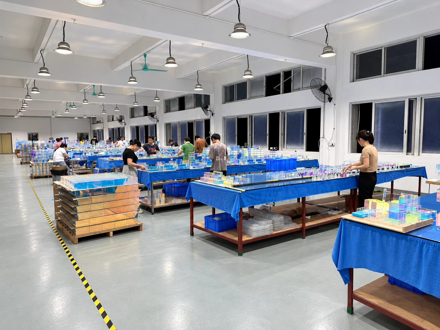 Workers assembling clear acrylic display components at blue-covered worktables
