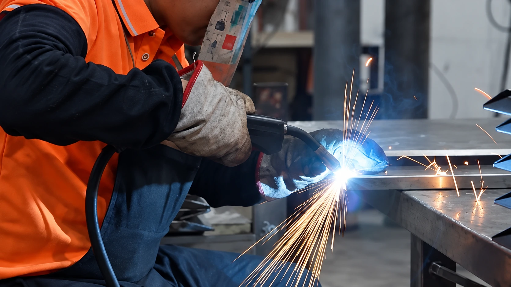 Gloved worker welding a metal frame at a fabrication workbench